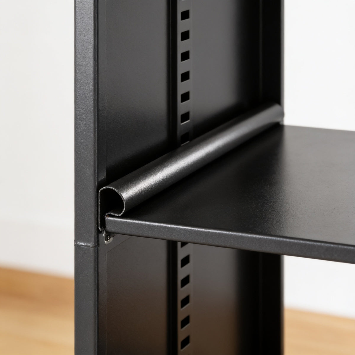 Close detail inside the cabinet showing the rolled front lip of a steel shelf and the shelf-height adjustment slots pressed into the side panel.