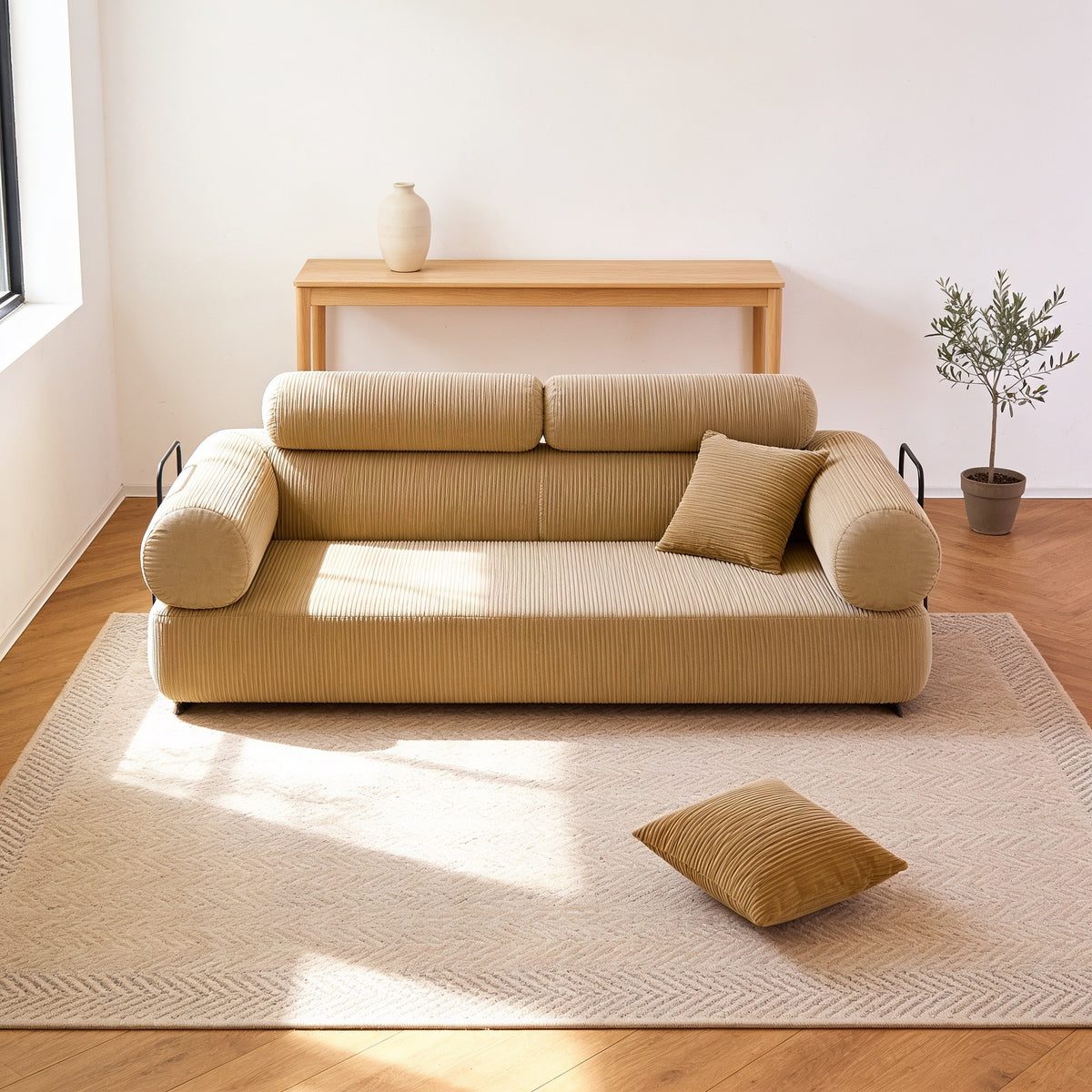 Beige corduroy folding sofa bed in sofa mode with rounded bolster arms, on an oatmeal rug in a warm living room.