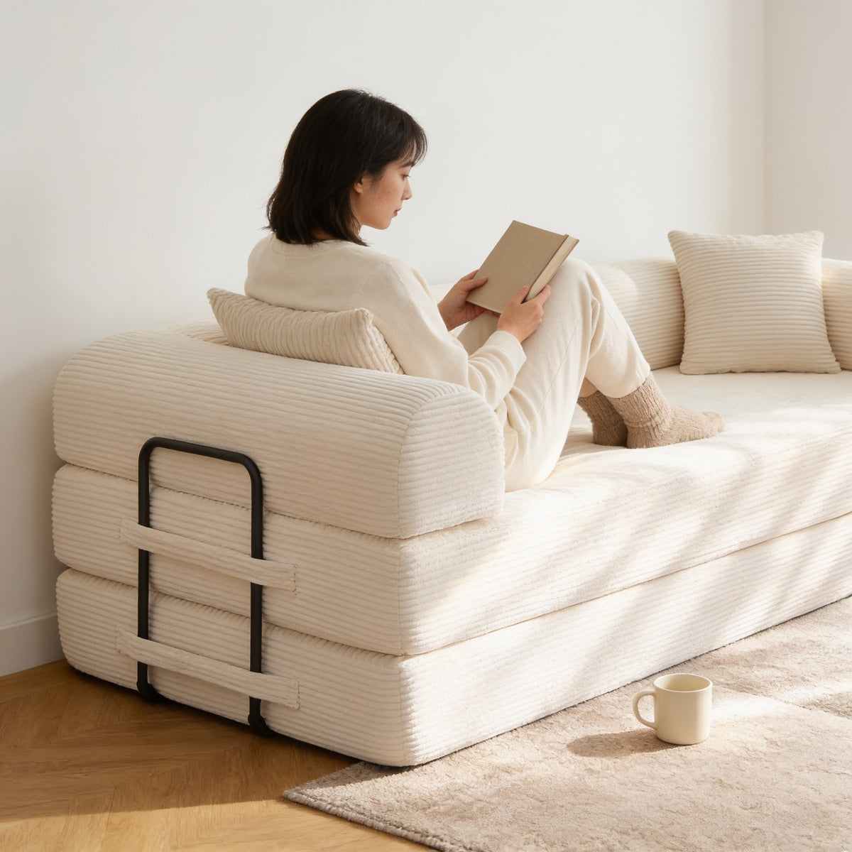 Adult sitting cross-legged well back on the beige corduroy sofa bed, reading, showing the deep sixty-seven centimetre seat.