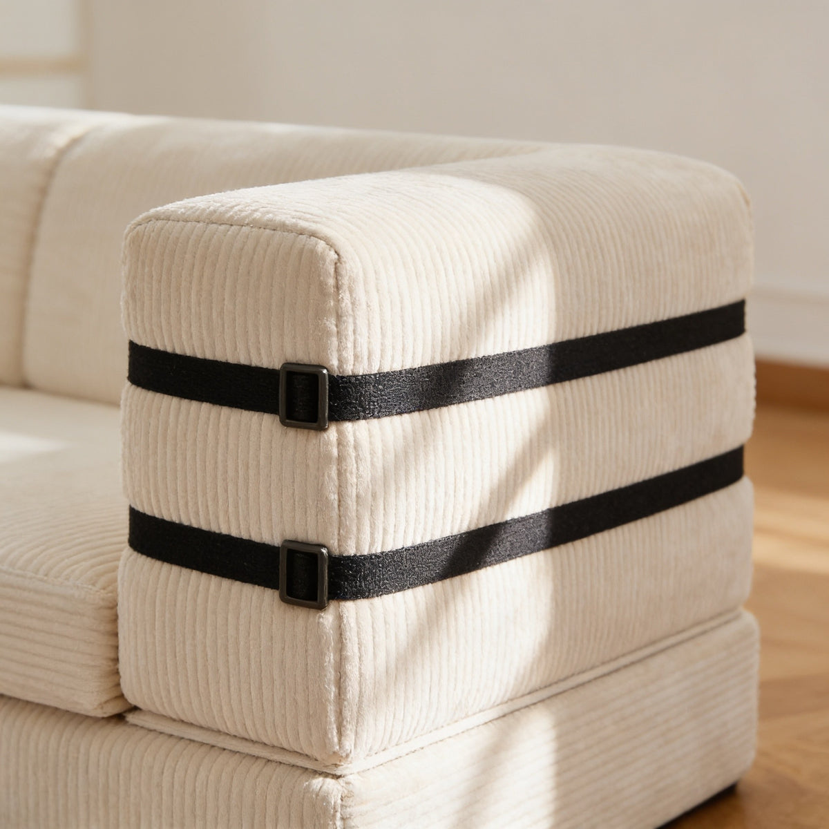 Close view of the sofa's straight foam armrest with two black webbing straps and dark metal loops across the outside face.