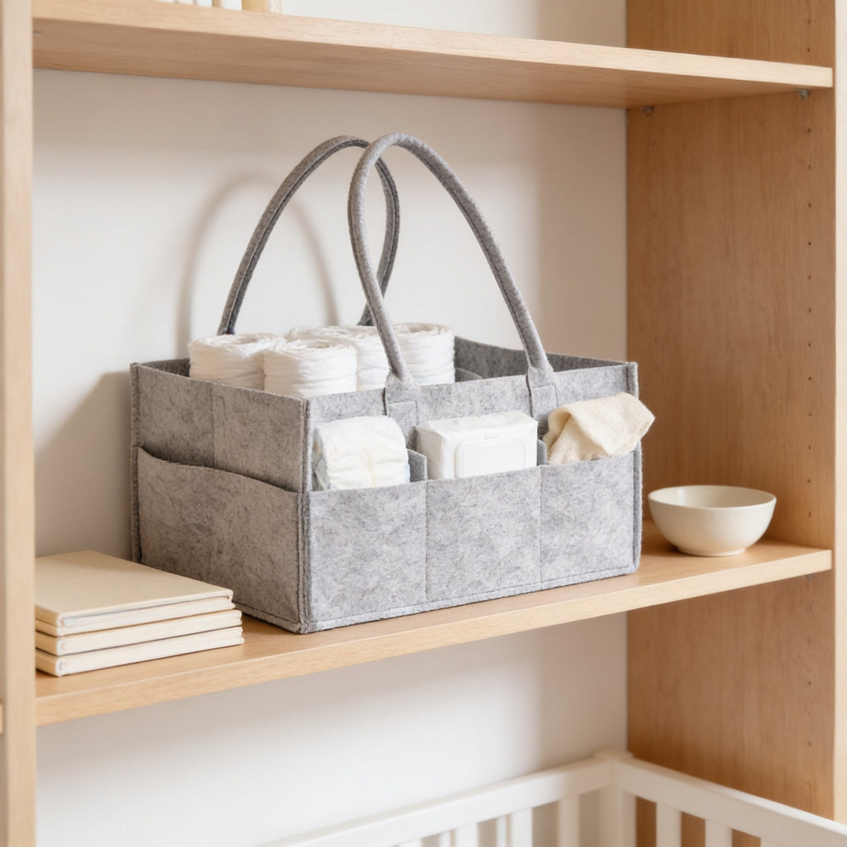Gray felt diaper caddy on a light oak nursery bookshelf beside board books.
