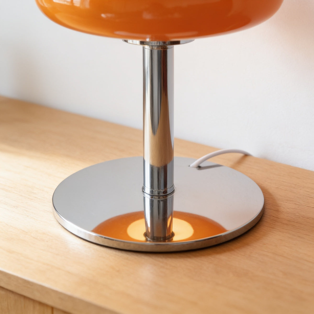 Close detail of the lamp's round polished chrome base and slim stem.