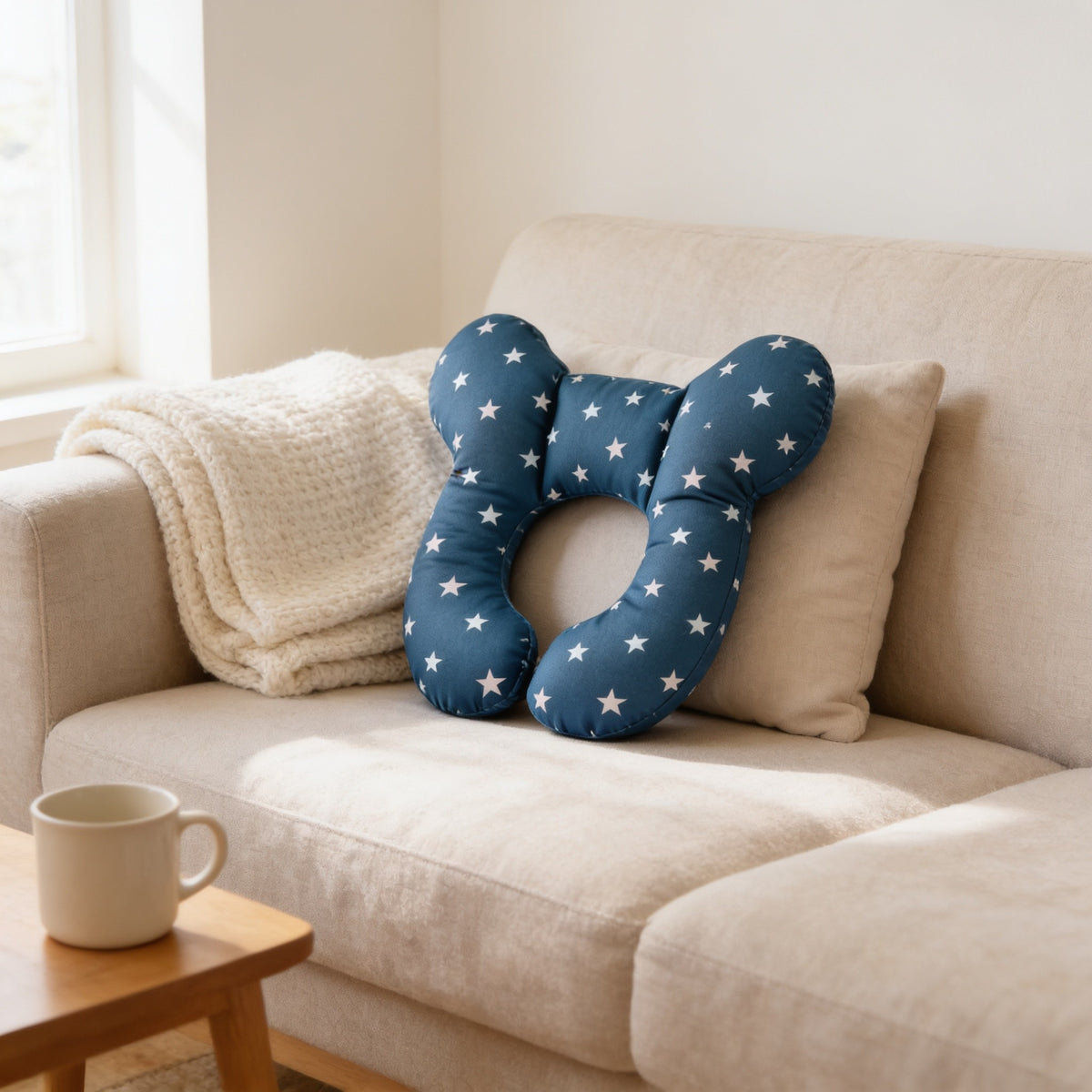 Navy star U-shaped toddler neck pillow resting on a linen sofa beside a mug, 25 by 26 cm.