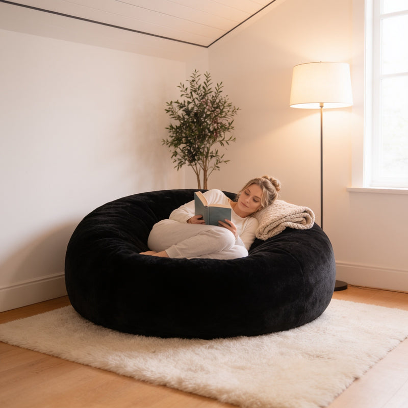 Black 4 ft plush foam bean bag chair with a woman reading in a cozy living room corner, 120 cm across.