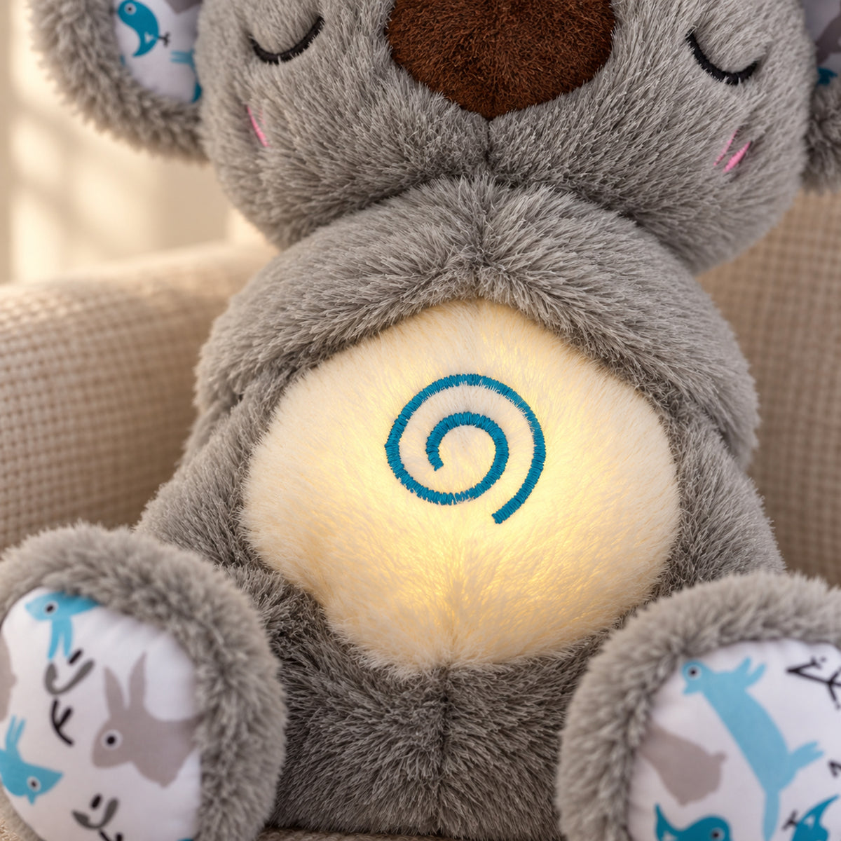 Close view of gray koala plush fibers and teal embroidered spiral on its cream belly