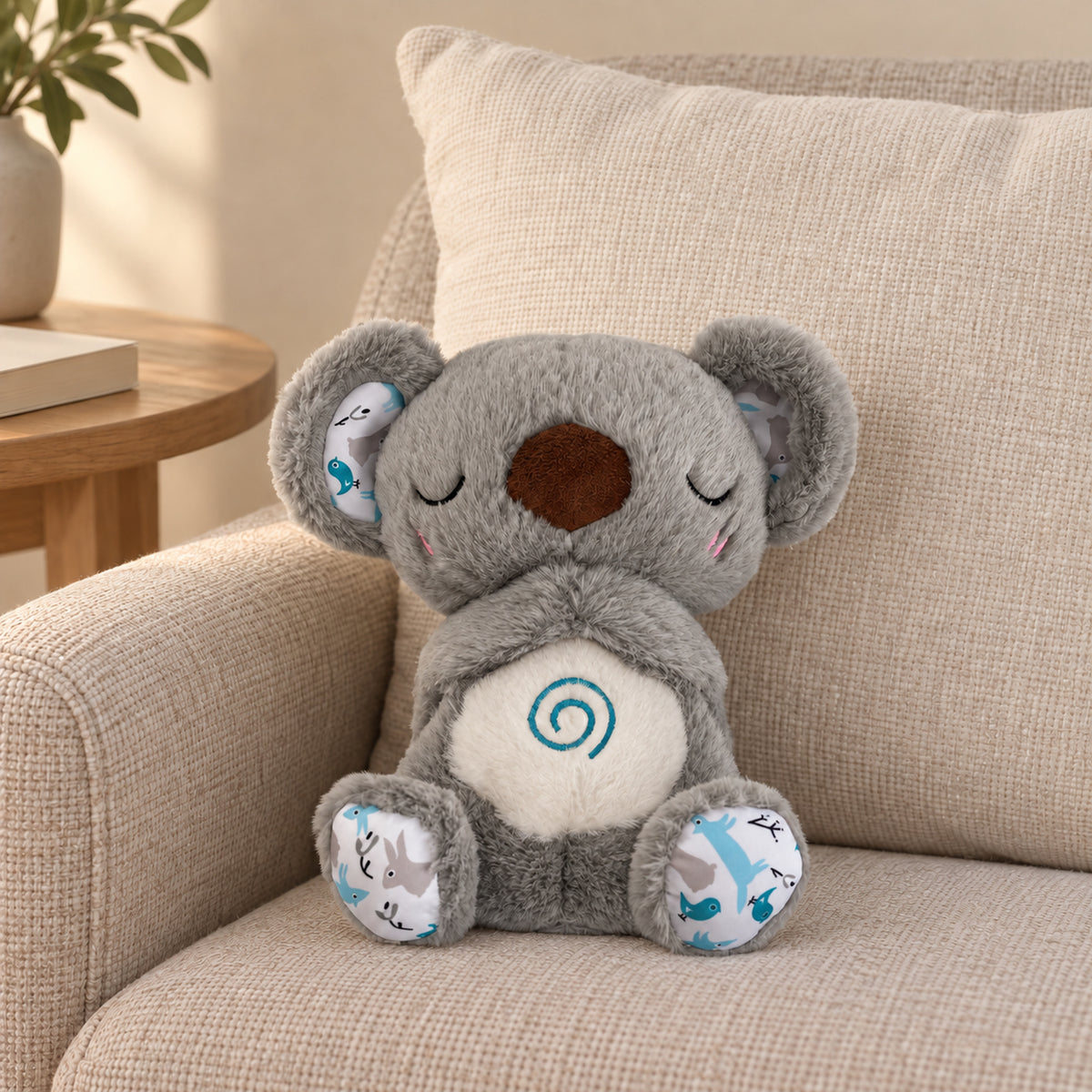Gray koala breathing plush showing its unlit cream spiral belly on a linen armchair