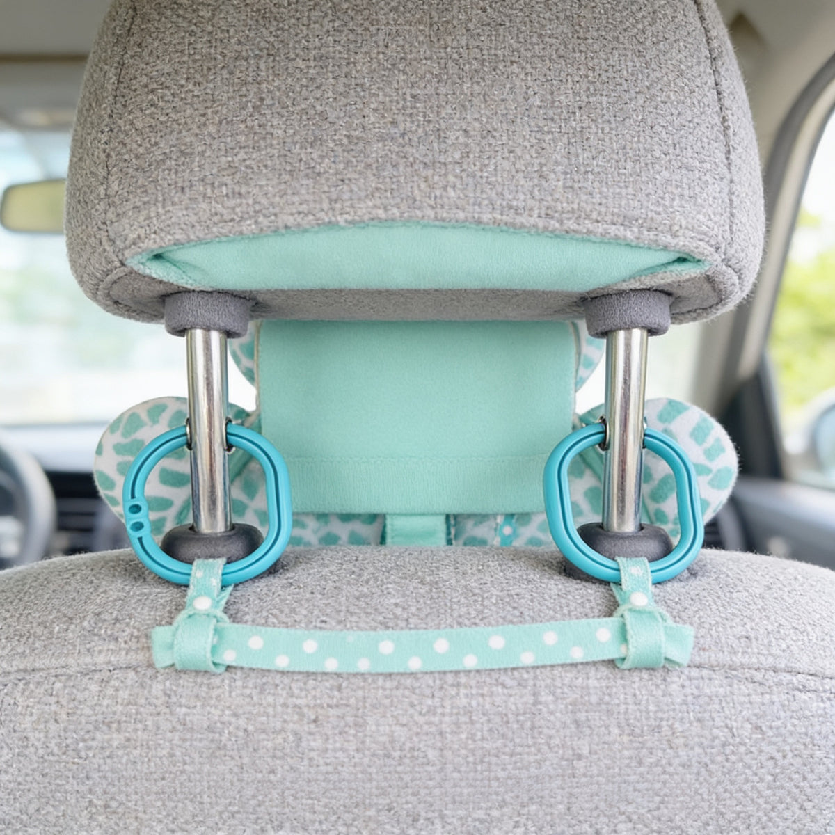 Back of the grey headrest showing the Deer car mirror's mint fabric panel, dotted strap and two turquoise clip rings fastened around the headrest posts