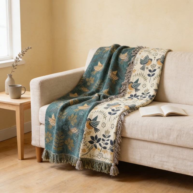 Teal bird cotton jacquard tassel throw draped over a cream linen sofa