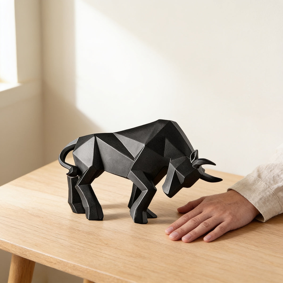 Black faceted bull statue on an oak table next to a hand for scale — Faceted Geometric Bull Statue