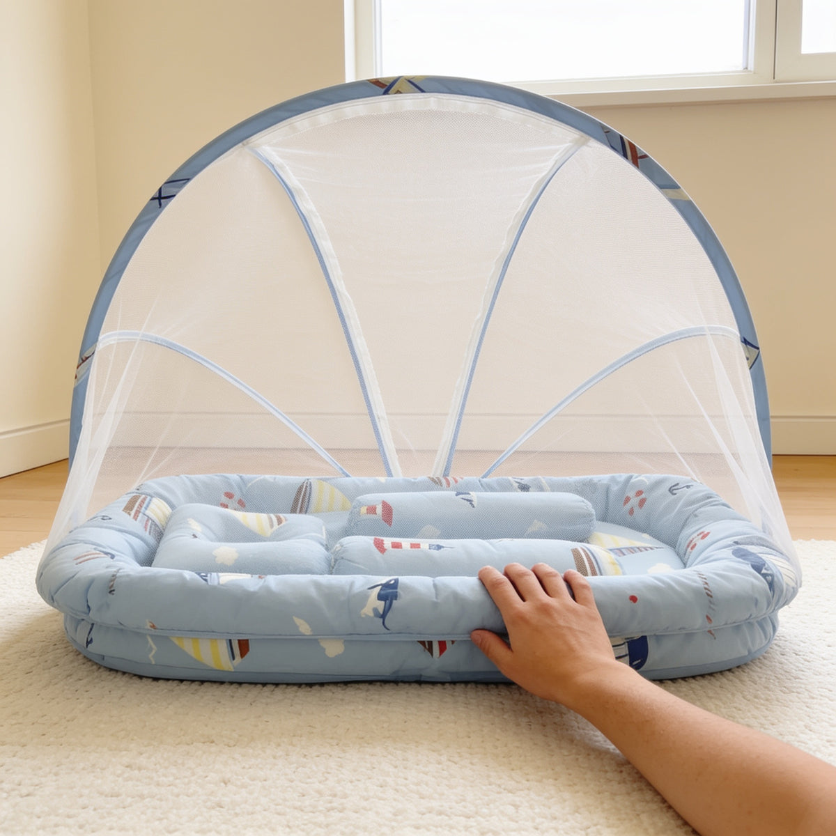 Adult hand resting on the padded rim of the Blue Nautical travel bassinet, showing its size on a living-room rug