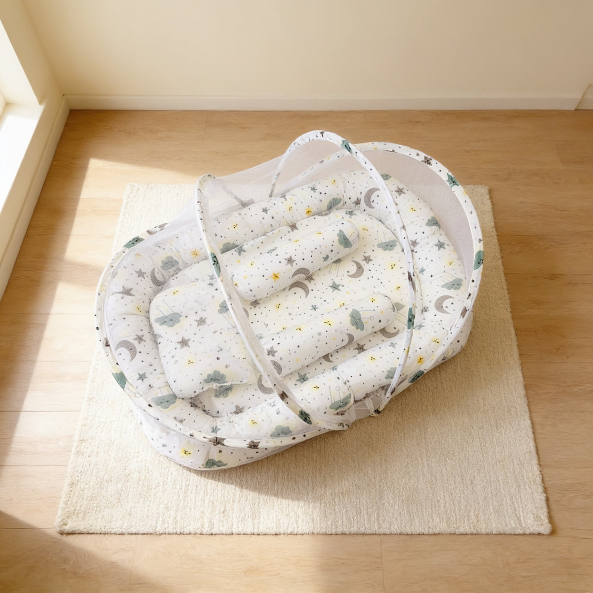 Cloud & Moon foldable travel bassinet, white cotton with clouds, moons and stars, with its mesh net dome up on a cream rug in a bright living room