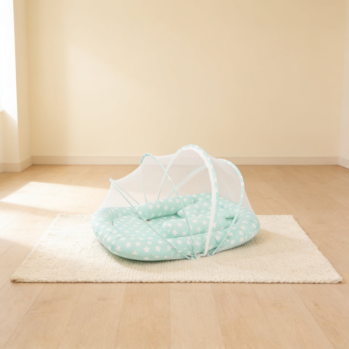 Mint Stars foldable travel bassinet, mint cotton with white stars, with its mesh net dome up on a cream rug in a bright living room