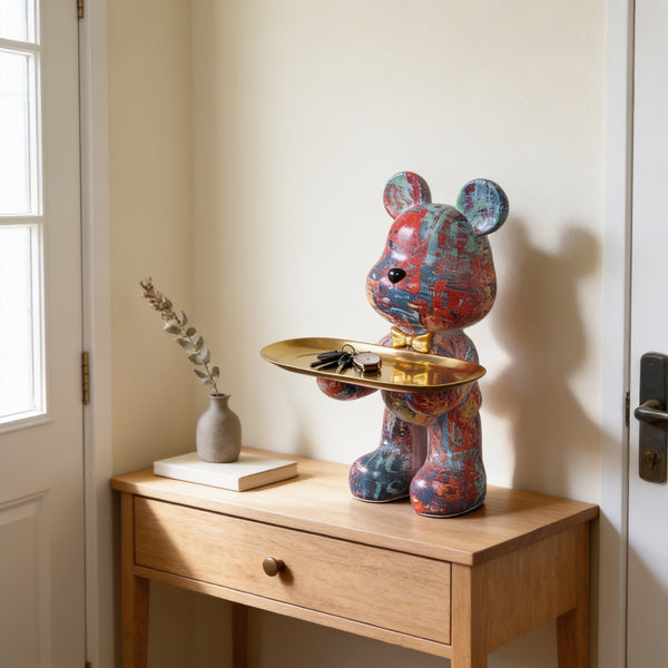 Pink and blue splash graffiti bear statue holding a gold tray on an entryway console