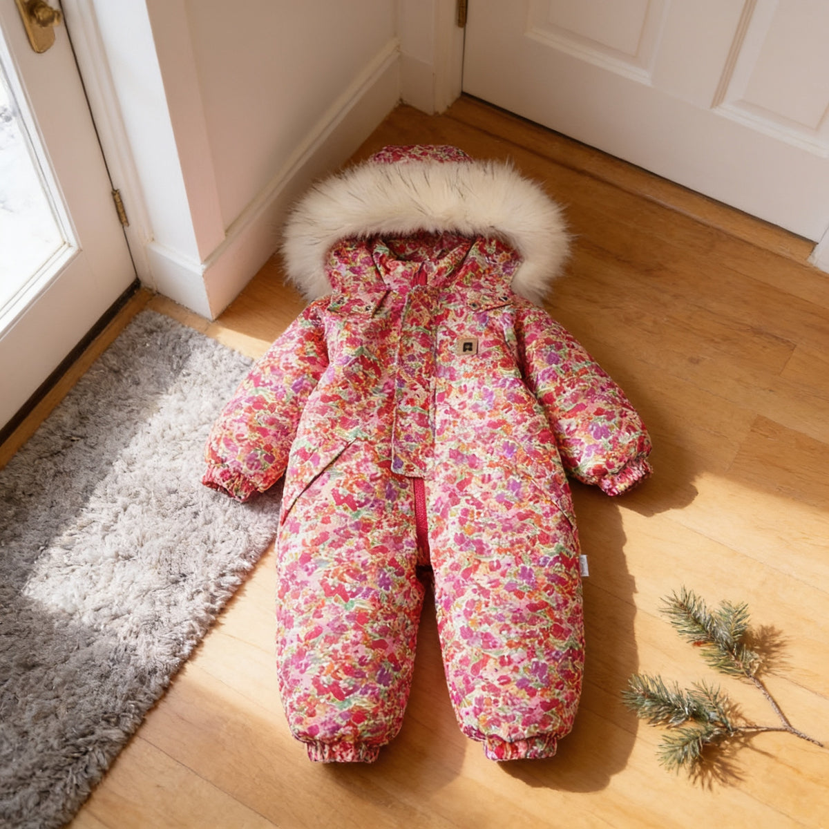 Floret hooded one-piece toddler snowsuit with a dense pink and red ditsy floral print, laid flat on the same entryway floor