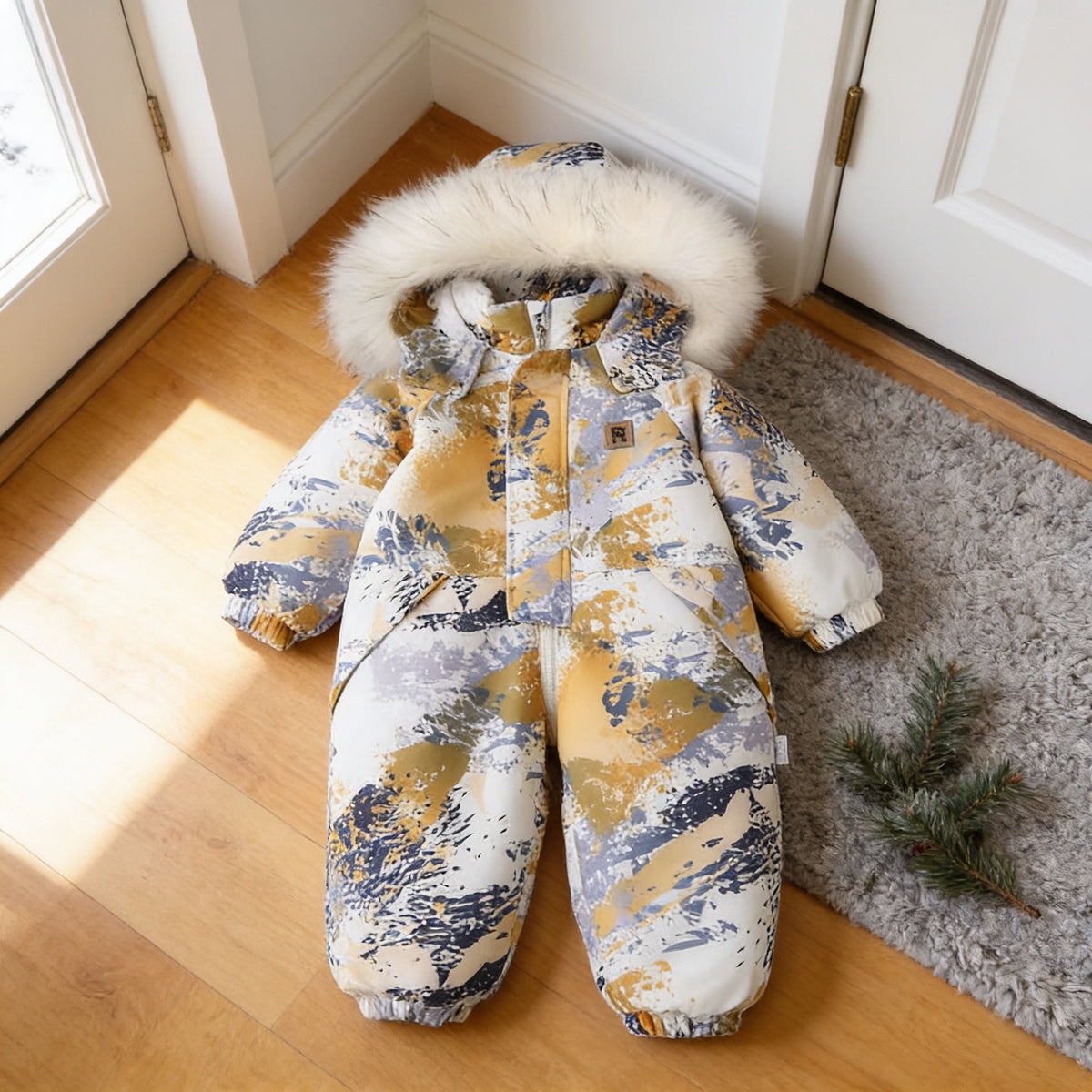 Mustard Camo hooded one-piece toddler snowsuit, white with mustard, navy and lavender-grey camouflage, laid flat on the same entryway floor