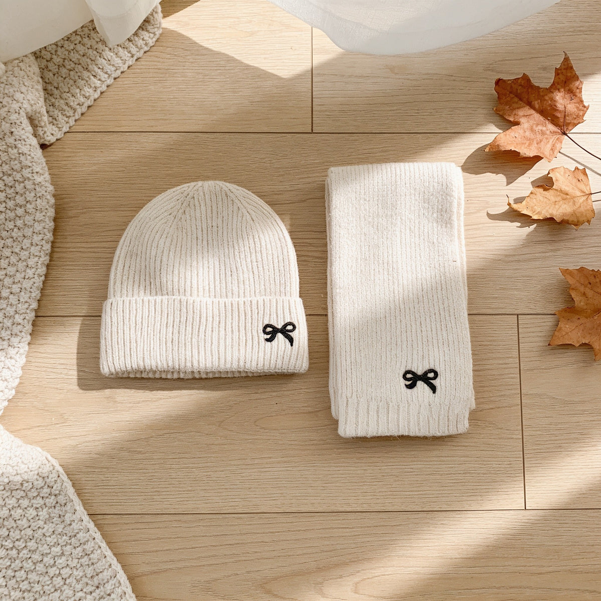 Cream ribbed knit kids beanie and scarf with embroidered bows, laid flat.