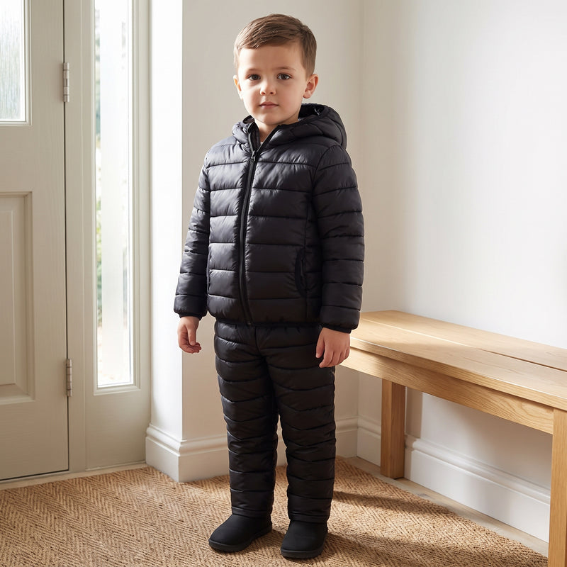 Child wearing the black quilted jacket and matching trousers in a home entryway