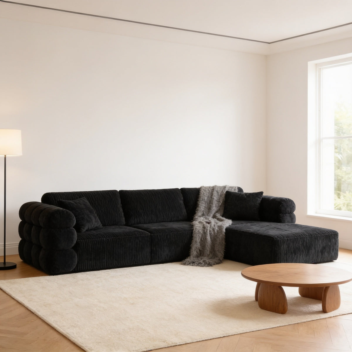 Black corduroy L-shaped boneless couch with chaise in a bright living room, 244 cm wide.