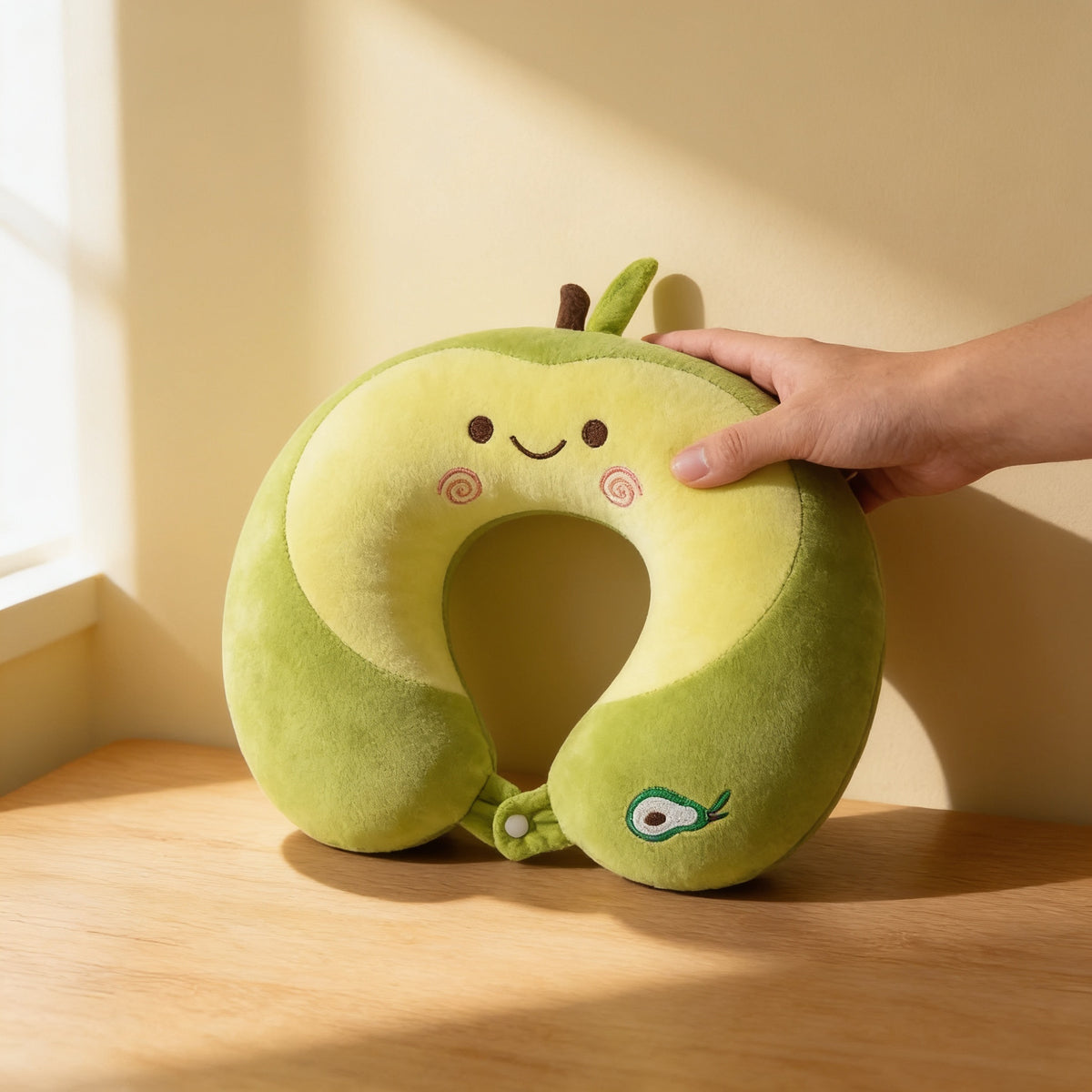 Green avocado memory foam travel neck pillow held in an adult hand on an oak table, showing its 30 cm width