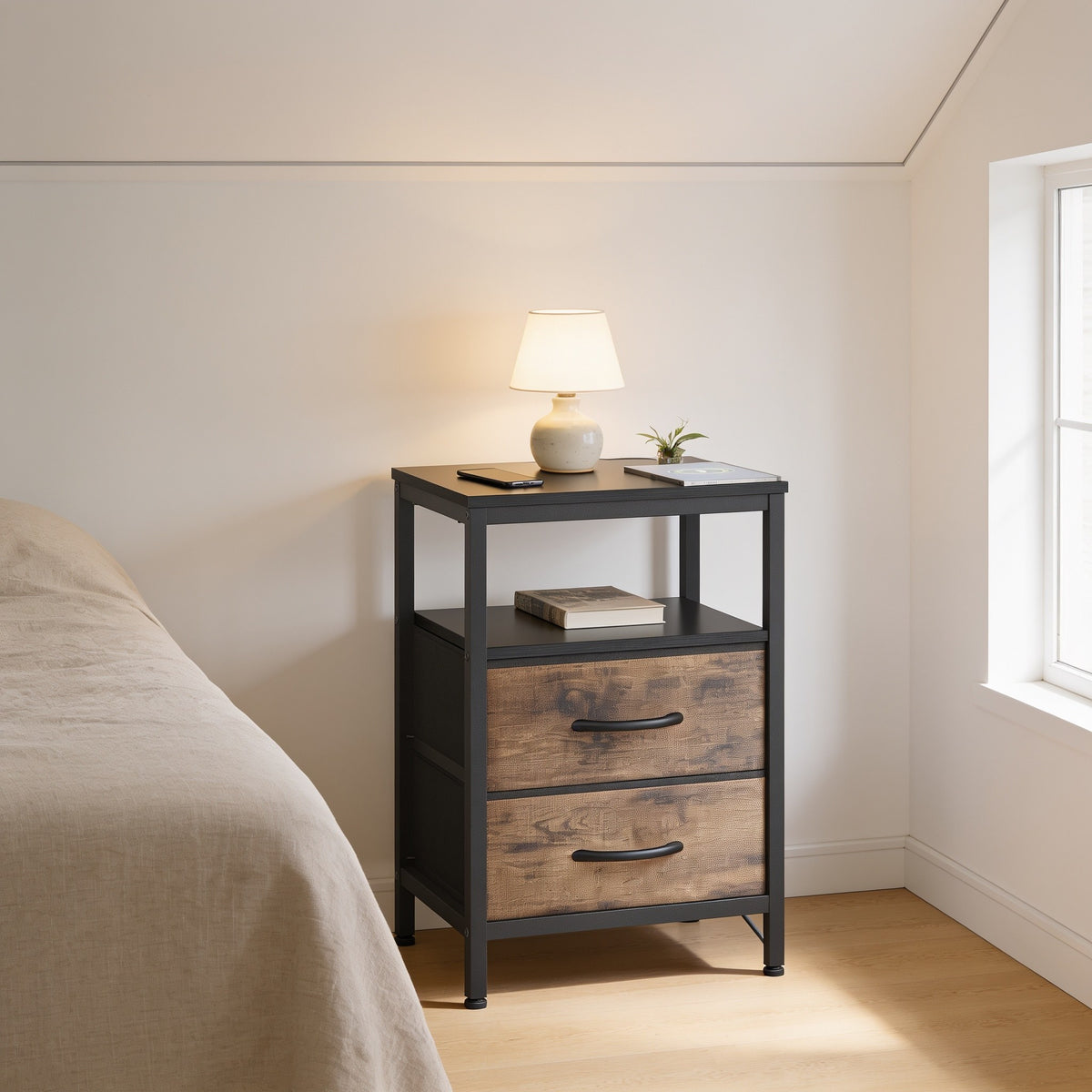 Black and brown nightstand with black top and wood-look fabric drawers beside a bed.