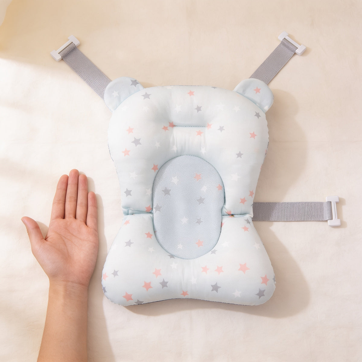 Blue Stars newborn bath cushion laid flat on cream linen beside an adult hand for scale, showing its 43 cm length and 28 cm wide leg end