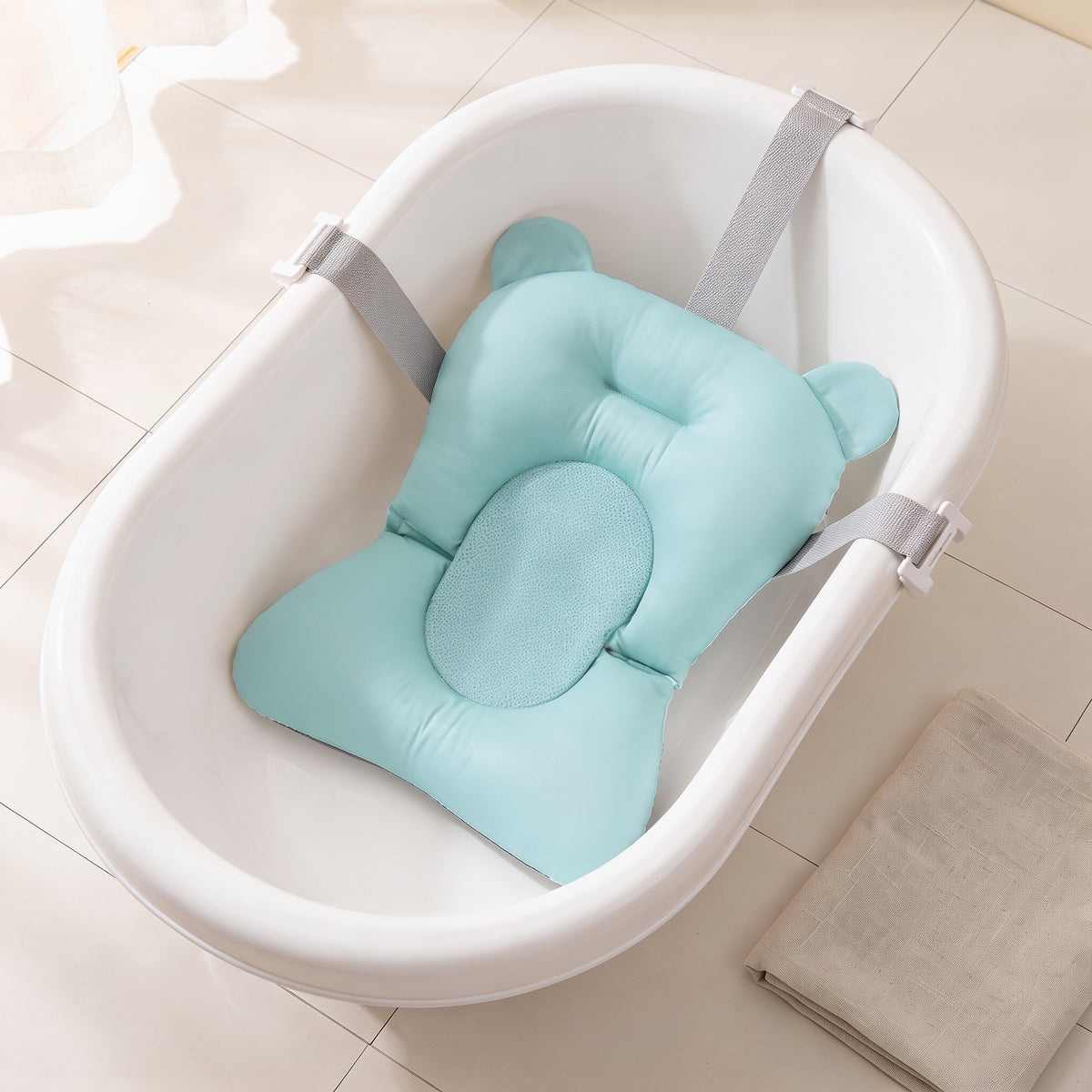 Aqua non-slip newborn baby bath cushion with a matching aqua mesh centre, fitted in the same empty white baby bathtub with its belts clipped over the rim