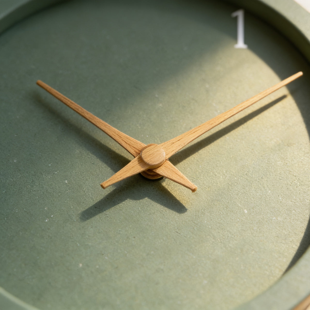 Close-up of the crossed wood-tone hands and speckled sage face of the wall clock