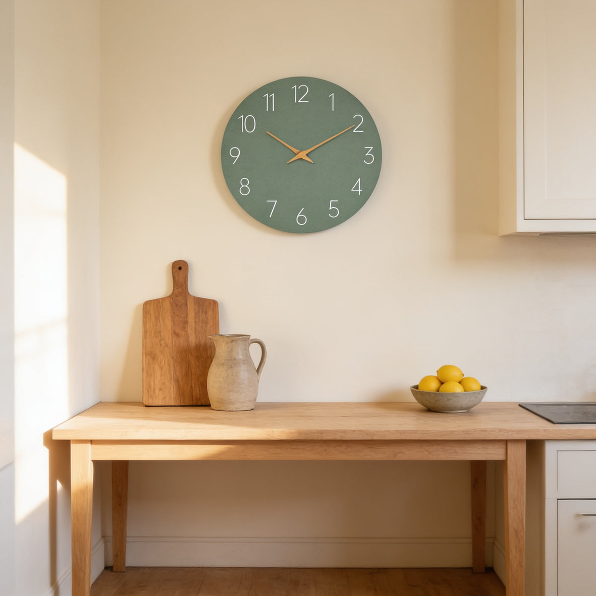 Sage green frameless wall clock on a cream kitchen wall above an oak worktop