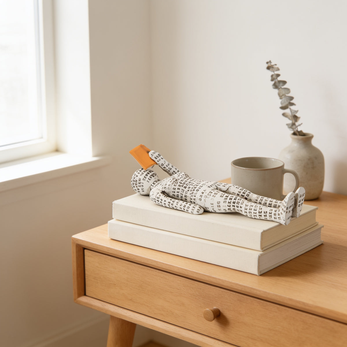 Lying paper-pulp reading figurine with orange book on stacked books — Paper-Pulp Reading Figurine