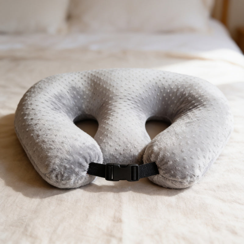 Gray minky dot twin nursing pillow with two curved cutouts and a buckle strap resting on a made bed.