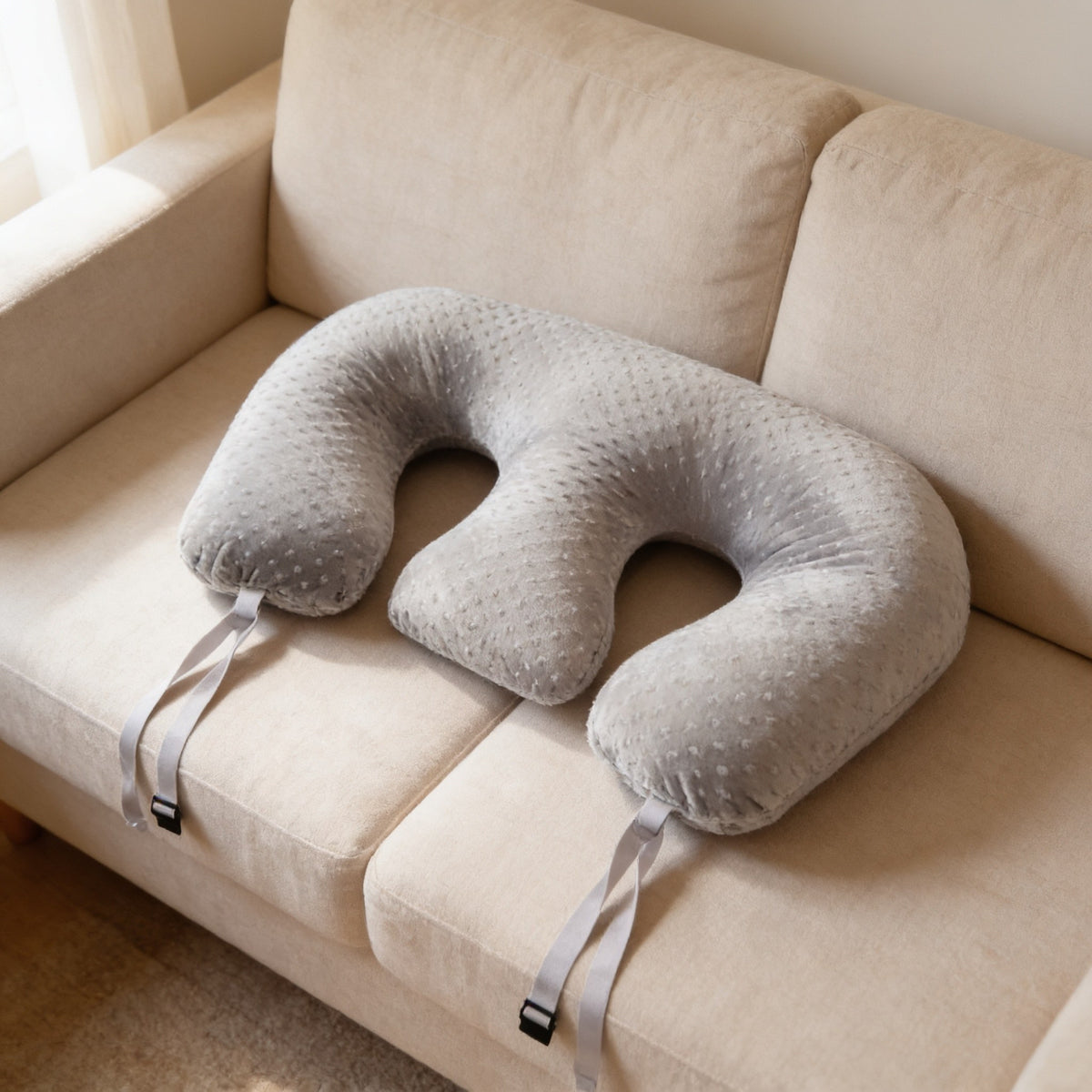 Gray twin nursing pillow on a linen sofa showing its two curved cutouts, 95 cm wide.