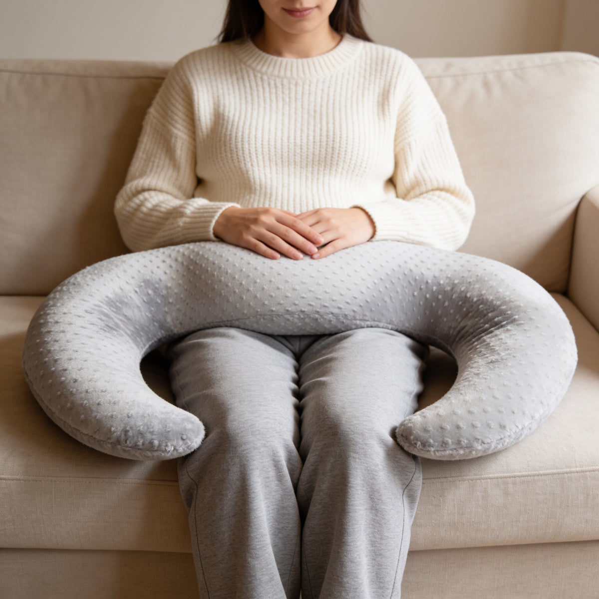 Adult seated on a sofa with the gray twin nursing pillow wrapped around her waist.