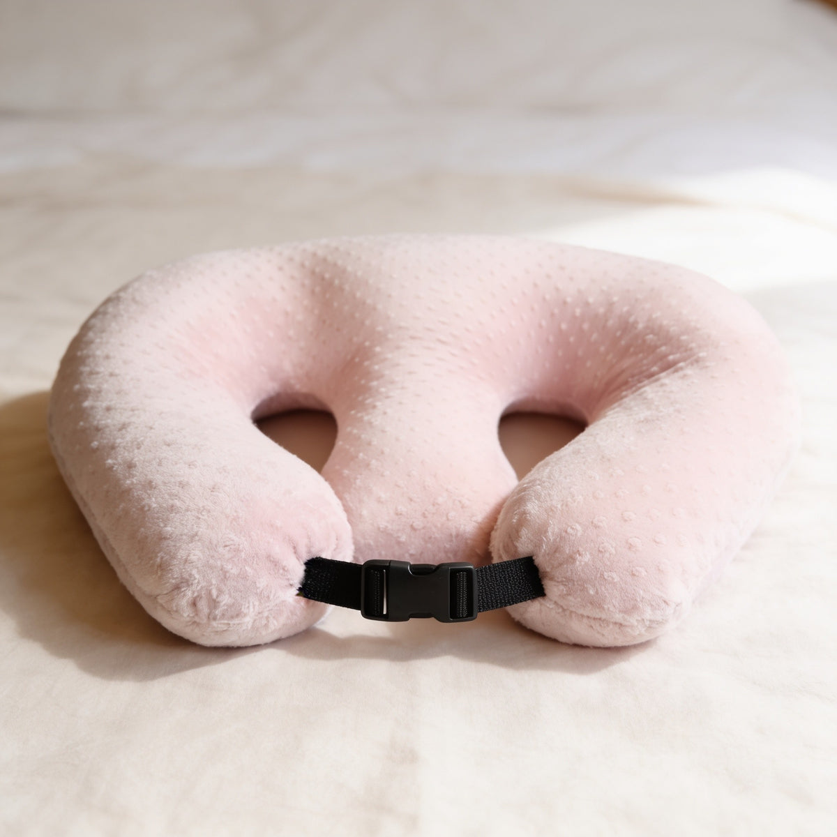 Pink minky dot twin nursing pillow with buckle strap on a made bed.