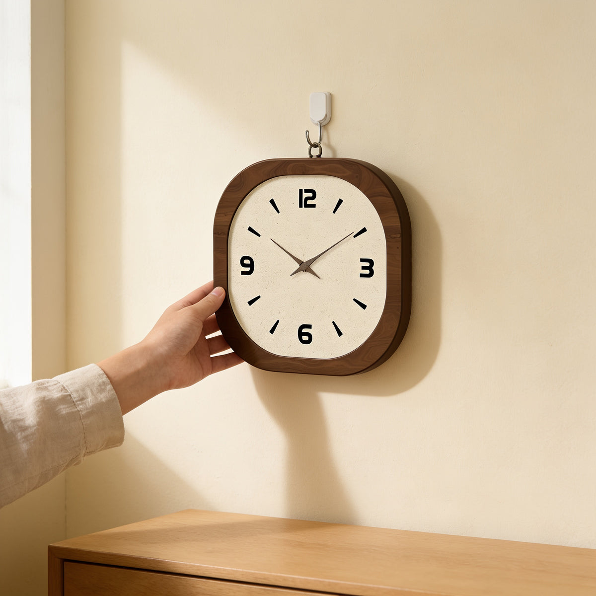 Hand hanging the rounded square wood wall clock on a cream wall — Rounded Square Wood Wall Clock