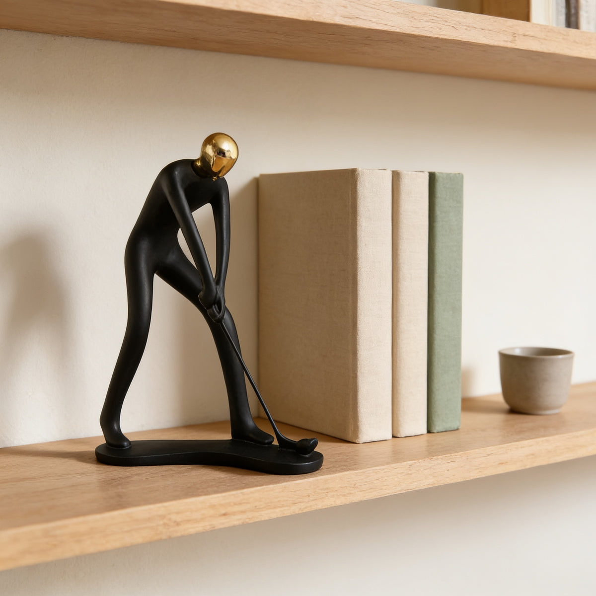 Black and gold putting golfer figurine on an oak bookshelf beside hardcover books — Black & Gold Sports Figurine