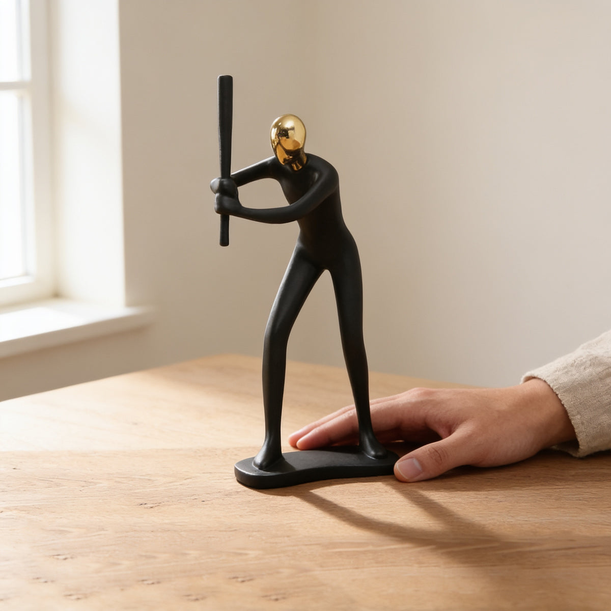 Black and gold baseball batter figurine on an oak table next to a hand for scale — Black & Gold Sports Figurine