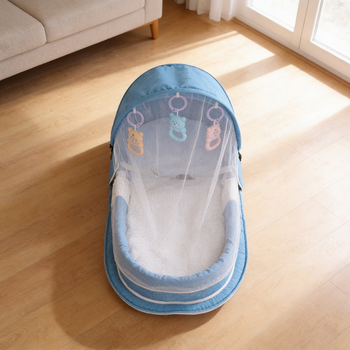 Travel bassinet from above with mesh net open, showing padded base and hanging toys.