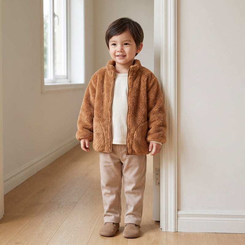 Toddler wearing the camel plush teddy fleece zip-up jacket in a home hallway