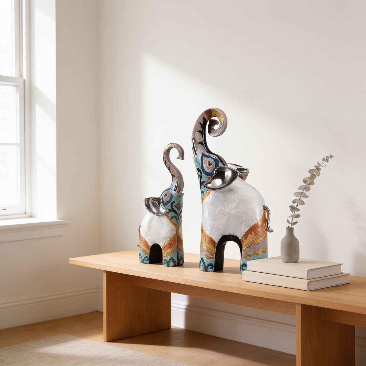 Large and small trunk-up elephant statues on an oak bench
