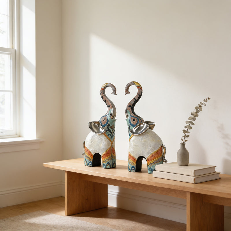 Matching pair of trunk-up elephant statues on an oak bench in a sunlit room