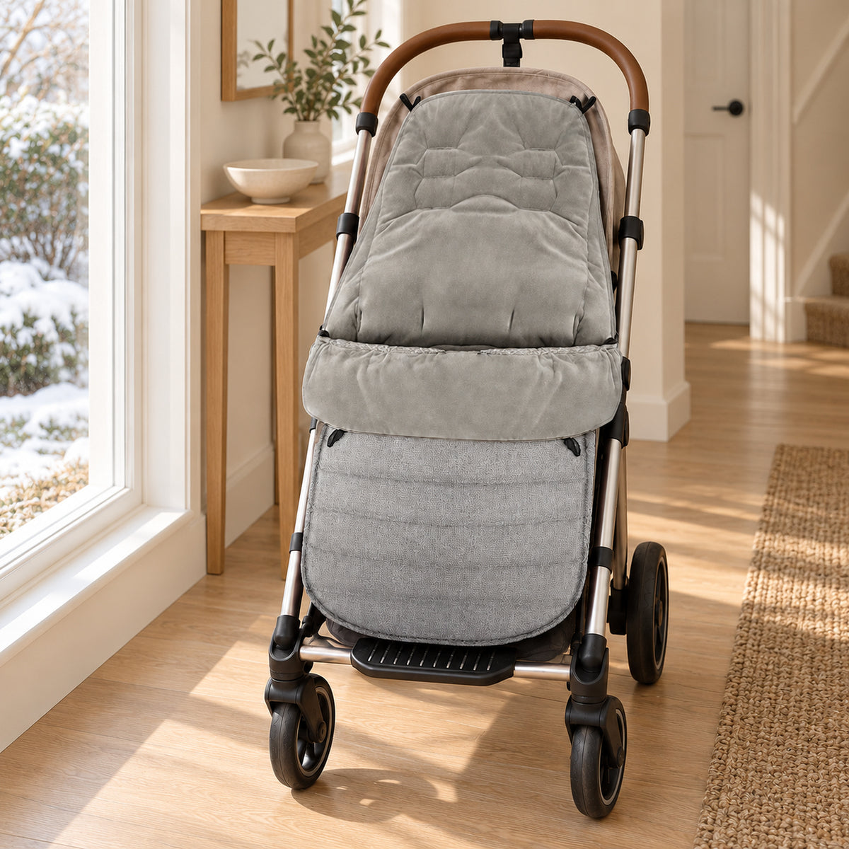 Gray stroller footmuff on an empty stroller beside a window overlooking a winter garden