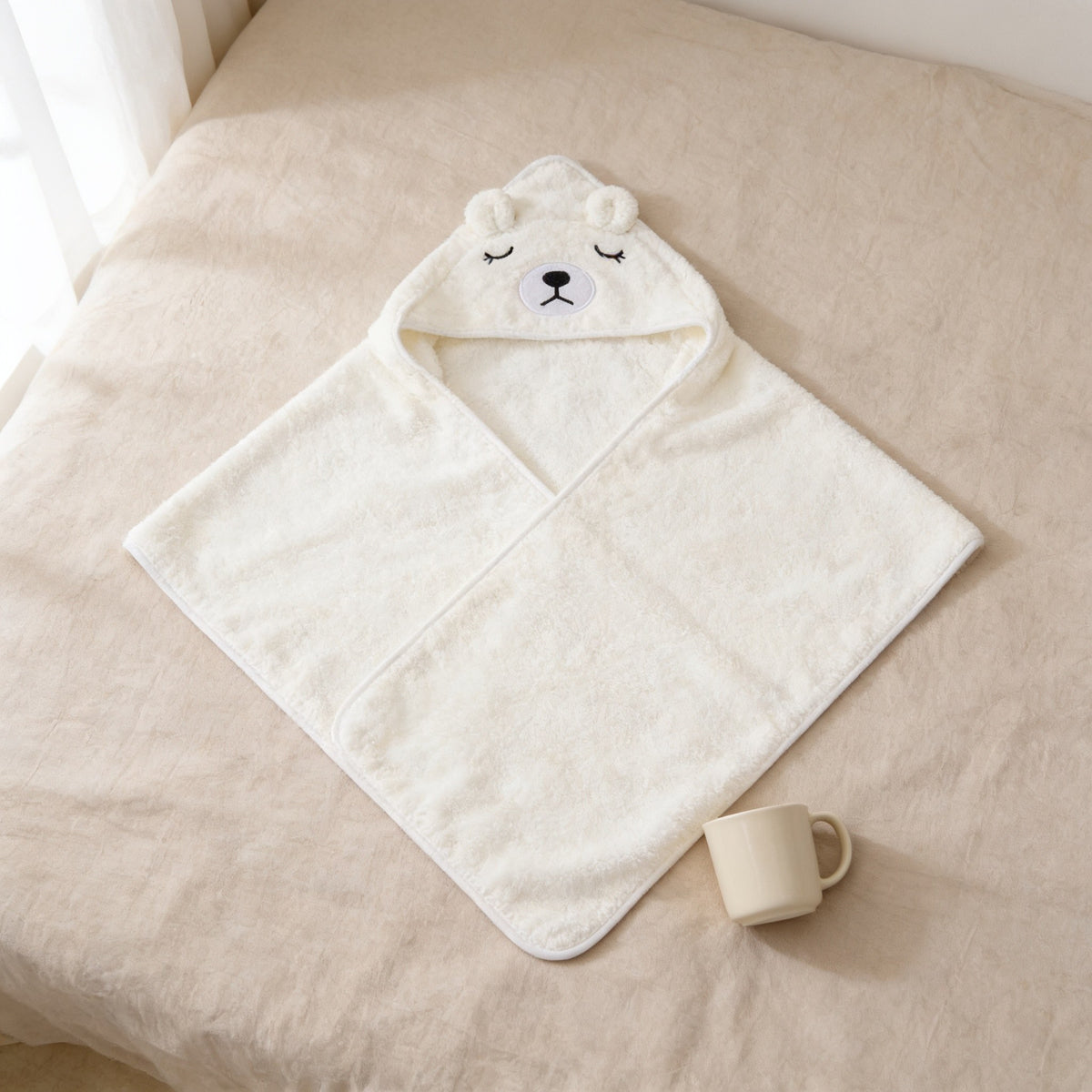Cream bear hooded towel laid flat on a bed, 80 by 80 cm.