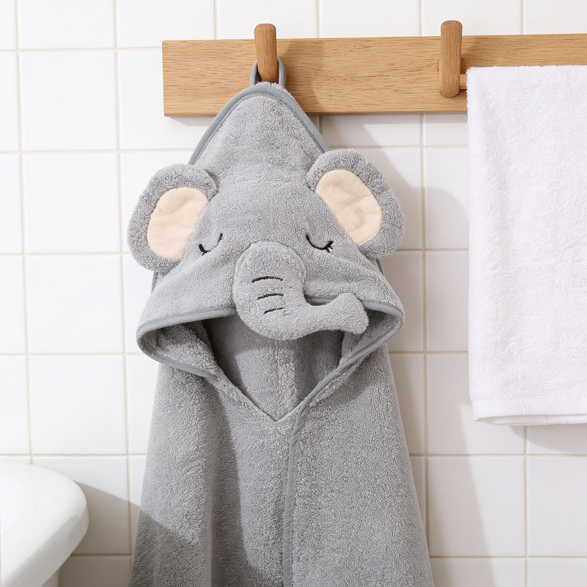 Gray elephant hooded baby towel hanging on an oak peg rail.