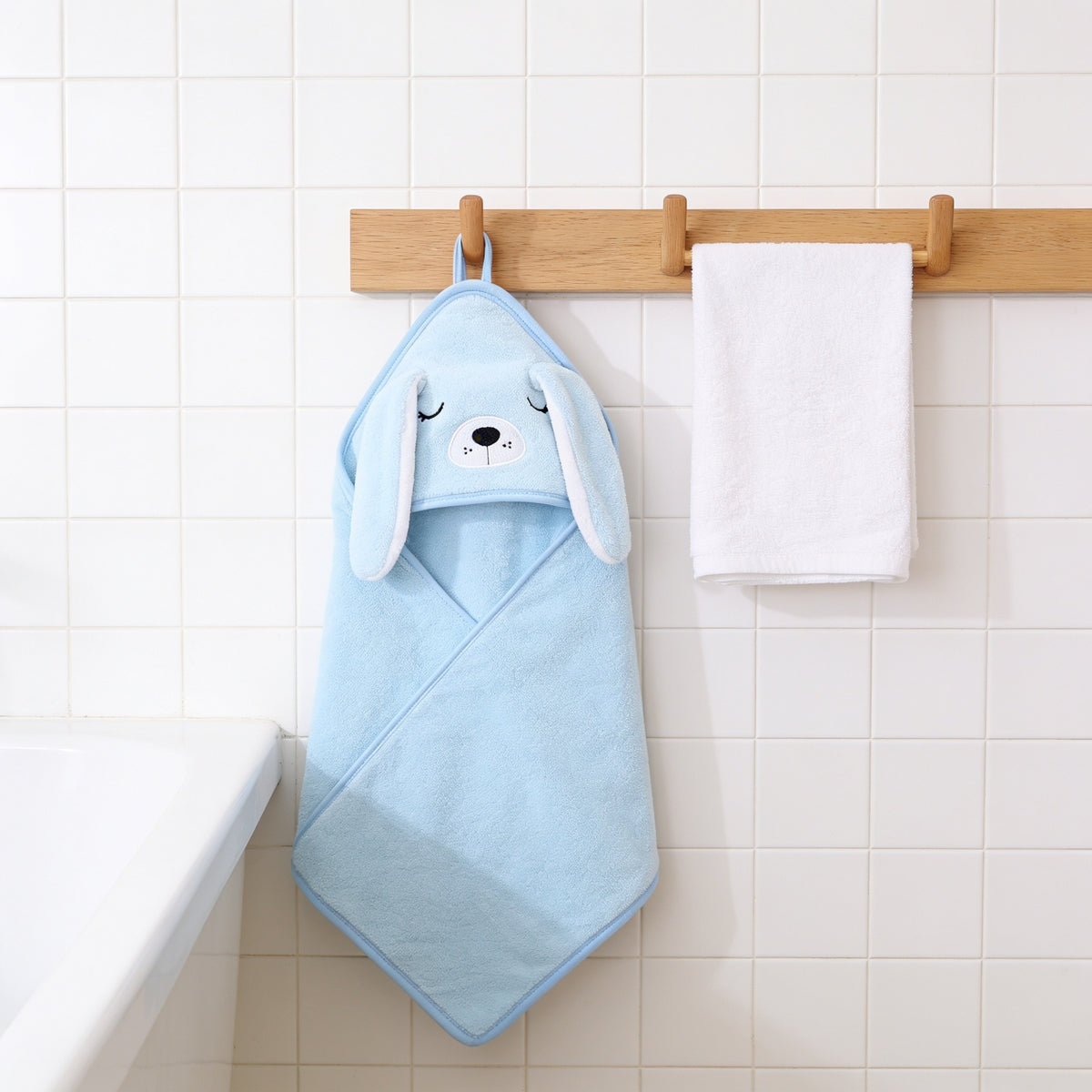 Blue puppy hooded baby towel with floppy ears hanging on an oak peg rail.