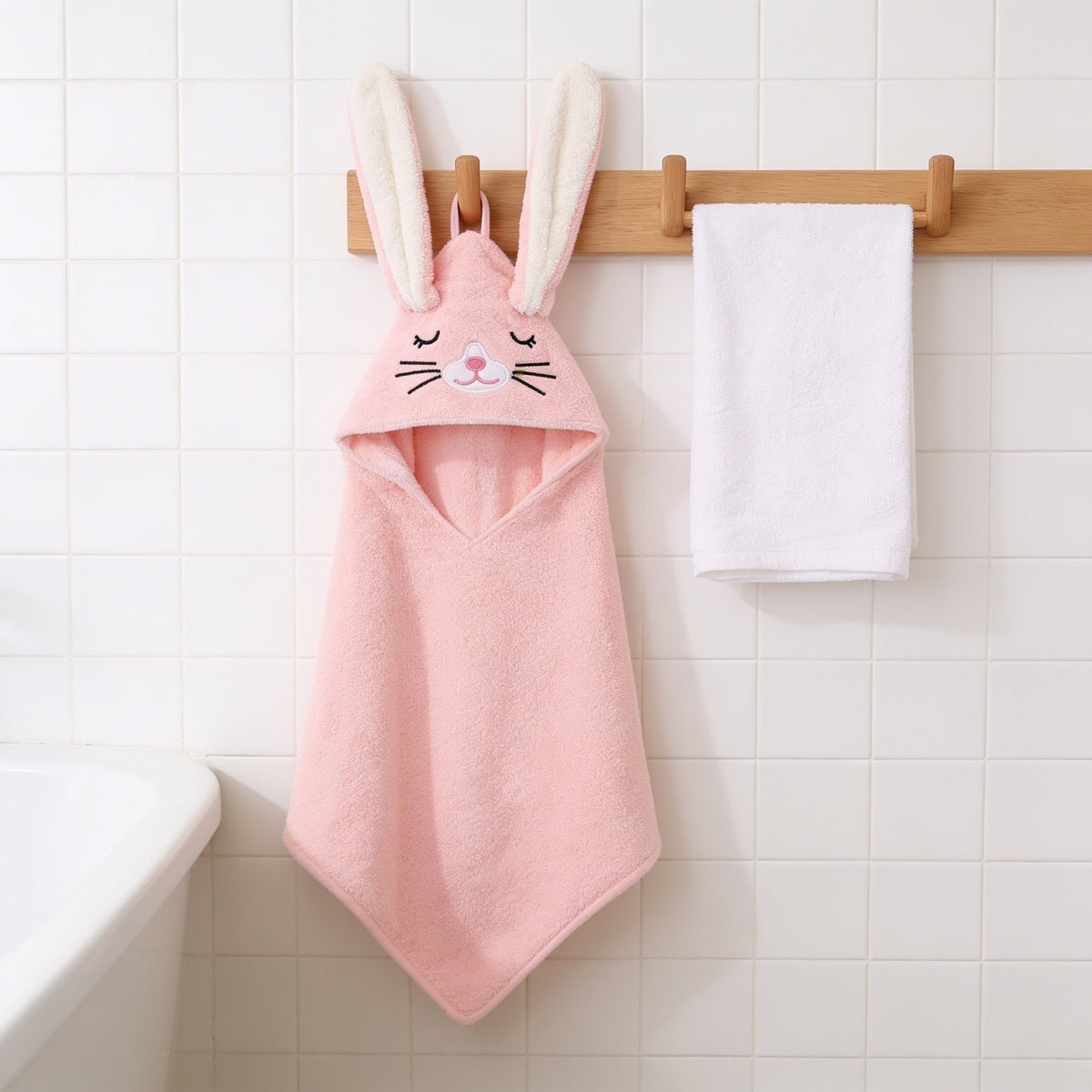 Pink bunny hooded baby towel with upright ears hanging on an oak peg rail.