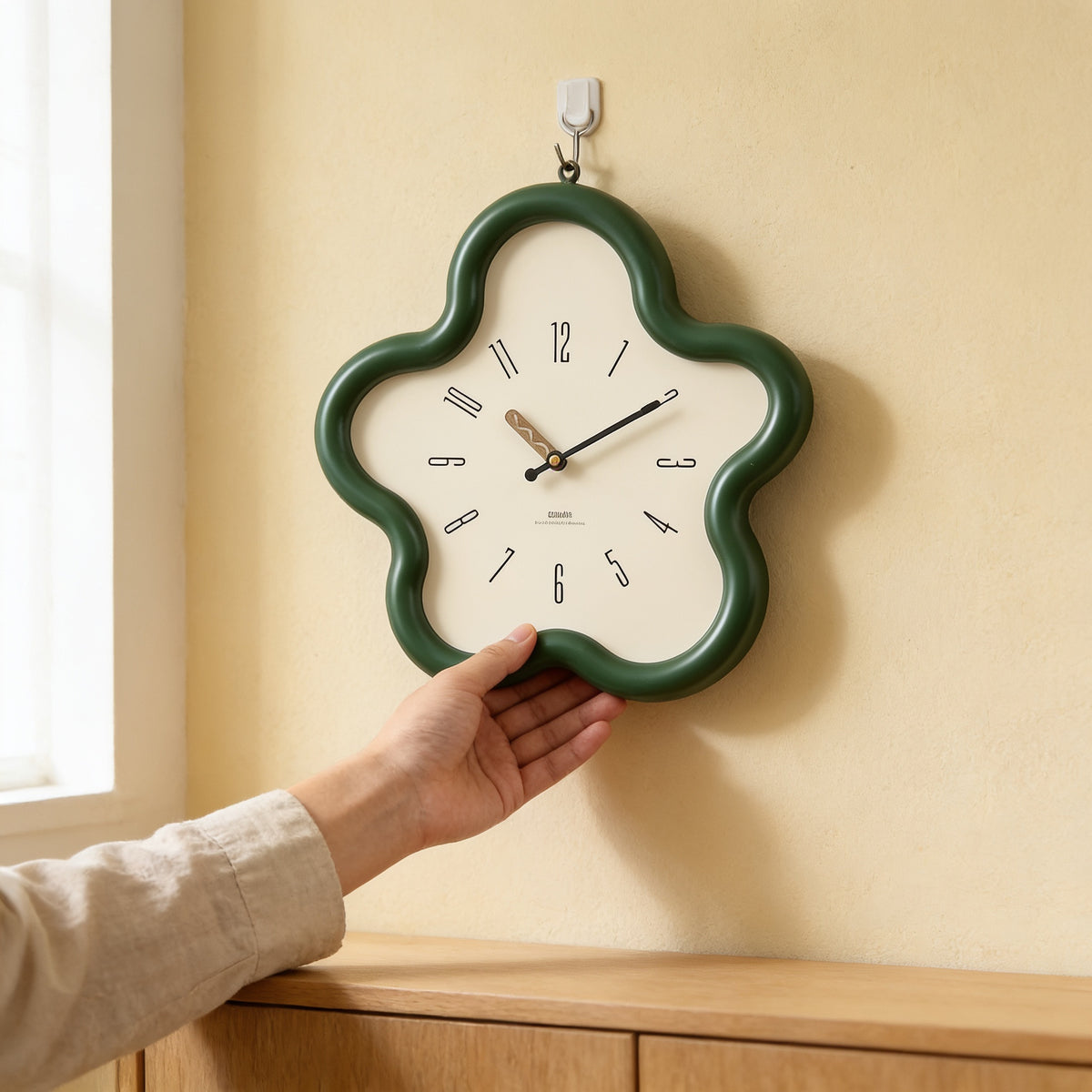 Hand hanging the green flower-shaped wall clock on a cream wall — Wavy Flower-Shaped Wall Clock