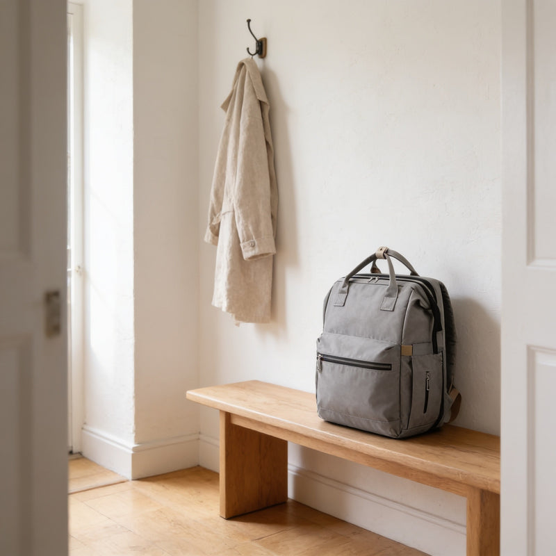 Gray diaper bag backpack standing on a light oak hallway bench.