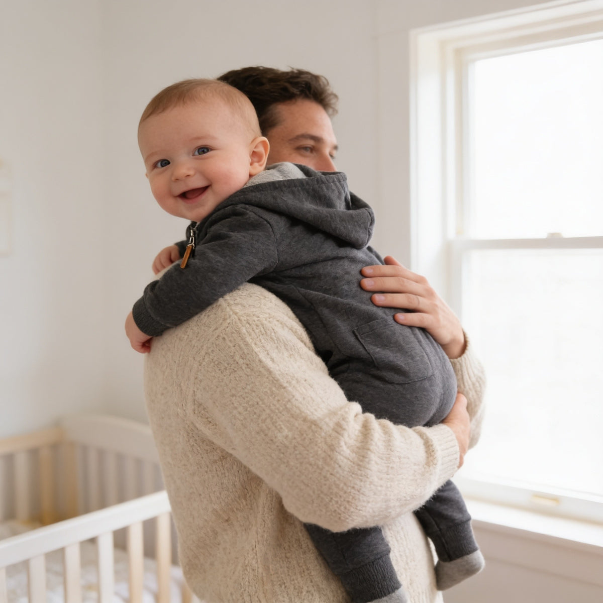 Parent holding a smiling baby in the charcoal hooded romper with the hood up.