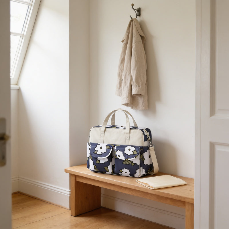 Navy floral print diaper tote bag with cream top band on a light oak hallway bench, its changing mat folded beside it.