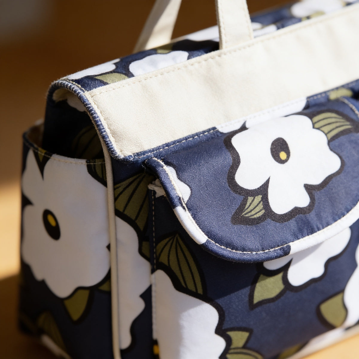 Close detail of the tote's navy floral print, piped pocket edge and cream band.